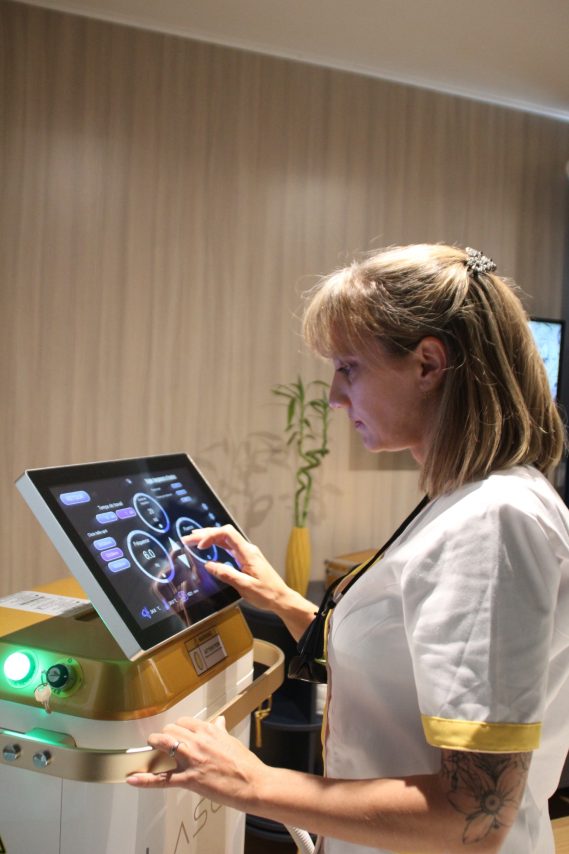 Réglages appareil épilation laser Femme en uniforme utilisant un écran tactile pour contrôler un appareil médical.